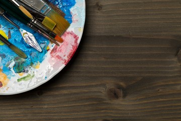 Artistic art supply utensils with brushes and colors palette on brown wooden background with copy space flat lay top view from above