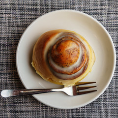Close-up top view of cinnamon bun on plate and fork. Coffee and dessert concept. Space for text.