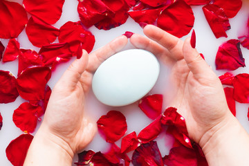 Female hands hold soap against the background of milk or white water with rose petals