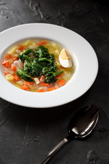 Healthy vegetarian meal with wild herbs. Homemade soup with stinging nettle and boiled egg in white plate on black background