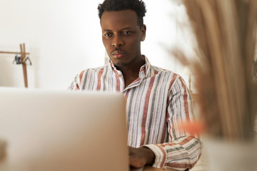 Serious young African man studying online on poartable computer, doing research or preparing for exam. Concentrated black student watching webinar on laptop, improving skills on programming