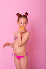 Caucasian beautiful little girl with fresh yellow lemons on a pink background.