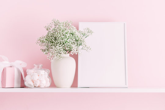 Home interior floral decor. Front view blank mock up of photo frame, beautiful flowers in vase on pink wall background.