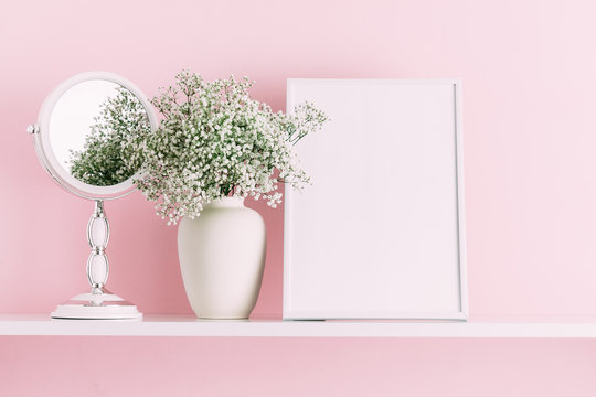 Home interior floral decor. Front view blank mock up of photo frame, mirror, beautiful flowers in vase on pink wall background.