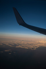 A VIEW OF THE PLANE'S WING AT SUNSET OVERLOOKING THE SKY AND CLOUDS