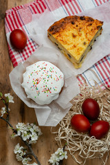 Easter cake, cheese casserole and Easter eggs in a wicker basket with a flowering branch on a wooden background