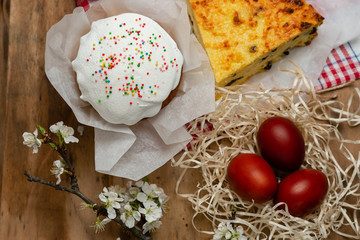 Easter cake, cheese casserole and Easter eggs in a wicker basket with a flowering branch on a wooden background