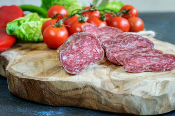 Sliced dry fuet with tomatoes cherry and some green on the wooden kitchen cutting board closeup. Mediterranean food.