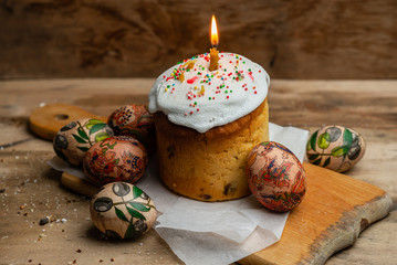 Easter cake with a burning candle, and Easter eggs on parchment paper on wooden board on a wooden background