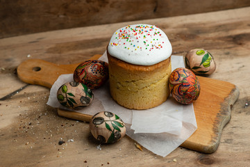 Easter cake, and Easter eggs on parchment paper on wooden board on a wooden background