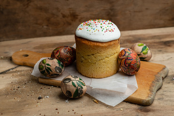 Easter cake, and Easter eggs on parchment paper on wooden board on a wooden background