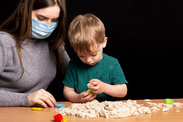 Mom in a medical mask and son play with kinetic sand. quarantine games.