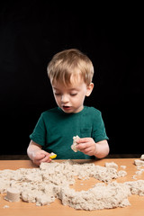 a three-year-old child plays with kinetic sand at home. Black background. isolate.