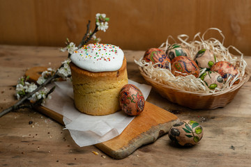 Easter cake, and Easter eggs in a wicker basket with a flowering branch on a wooden background