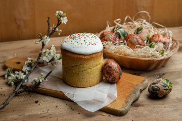 Easter cake, and Easter eggs in a wicker basket with a flowering branch on a wooden background