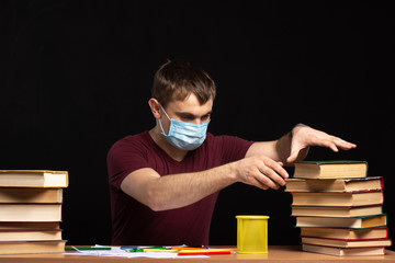 a young man in a medical mask selects a book from a pile. quarantined training. Black background.