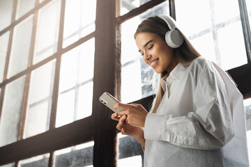 Fototapeta premium Pretty young girl in wireless headphones listening to music on smartphone. Online apps for mobile devices