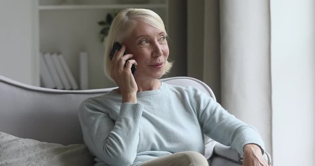 Happy middle aged woman relaxing on cozy sofa, talking on smartphone with friends. Excited elderly lady chatting sharing news on mobile phone with grown up children, resting in living room alone. - Powered by Adobe