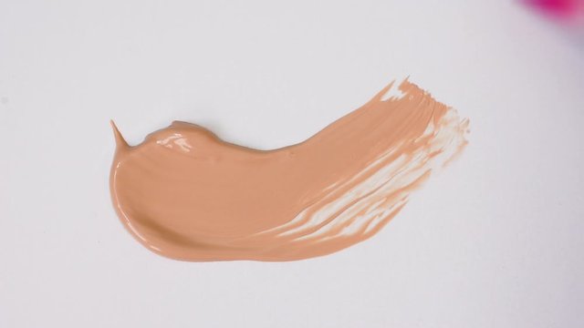 Delicate Light beige smear of tonal foundation on white background. Pink tone smudge with a brush. Beautiful pastel BB cream. Cosmetic products for makeup and skin care. Cosmetology. Closeup.