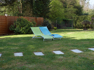 empty blue and yellow beach chairs in the garden on a green lawn in the background of the tree and wooden fence © Christof
