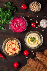 Plate of spicy traditional hummus with pepper and greens on a wooden background. Colorful hummus bowls decorated with chickpeas, herbs, garlic, tomate , crispy bread and chili pepper. Top view