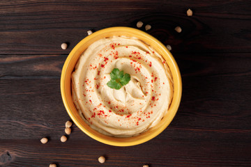 Plate of spicy traditional hummus with pepper and greens on a wooden background. Top view.