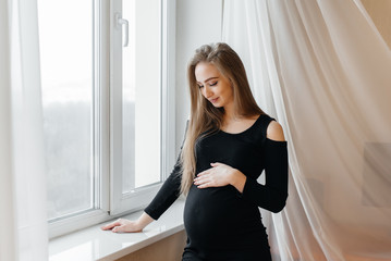 A beautiful pregnant girl is standing in a room near the window