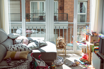 Untidied lounge room with many many toys on a grey sofa and on the floor on a urban flat