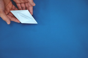 Hand releasing a white paper boat on a calm blue sea background. Letting go and acceptance concept. Top view, flat lay with copy space.