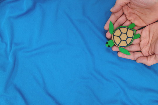 Human hands releasing a green sea turtle on a blue sea background. Paper cardboard cutout, top view, flat lay. Marine wildlife conservation concept.