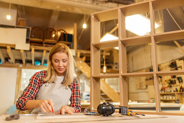attractive professional woodworker or craftswoman during work in factory, woman deals with wooden pieces, make wooden furniture for customers