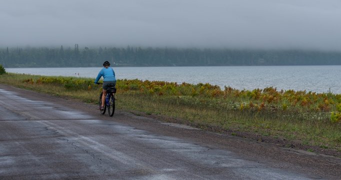 A Woman Bikes Along A Country Road Along Lake Superior In Michigan