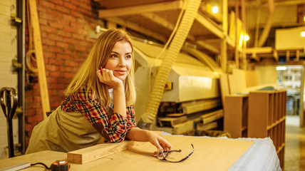 smiling carpenter woman at work, lady has her own workshop of making furniture for customers. professional cutting, drilling and projecting wooden handicraft