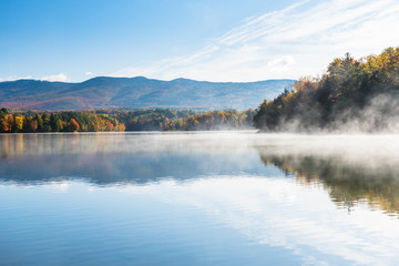 Fototapeta na wymiar Majestic mountain lake partly covered in morning fog in autumn. Stunning autumn colours.