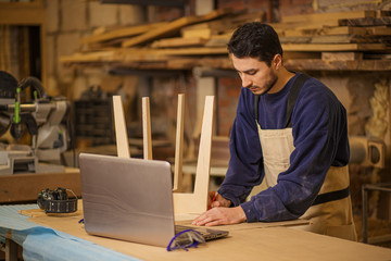 hardworking young woodworker marks wooden chair with a pencil, man make furniture on an order in...