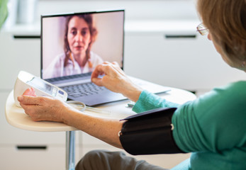 telemedicine concept elderly woman speaking to her doctor online and taking her blood pressure