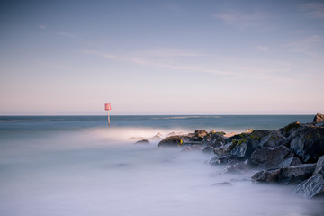 a long exposure image of waves breaking over rocks at sunset with a clear horizon