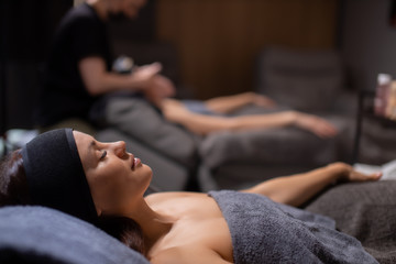 Obraz na płótnie Canvas side view on calm relaxed caucasian woman lying in wellbeing salon before skin treatment, woman get face lift massage in the background