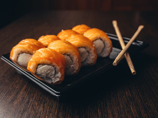 Food delivery, Philadelphia rolls in a black box with chopsticks. Brown wood background.