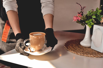 hands of a waitress in medical gloves with a coffee mug, in a cafe, virus, medical safety pandemic
