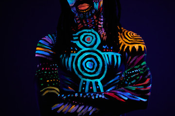 portrait of african male with fluorescent body art glowing in neon lights in dark space. fashion model with naked skin