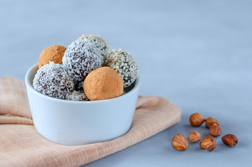 Raw vegan energy balls in a bowl with nuts on a blue background. Natural sweets made from nuts and dried fruits in coconut and cocoa, close-up. The concept of paleo diet, sweets without sugar and