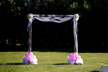 simple DIY wedding arch draped with white cloth and balloons at base in green field.