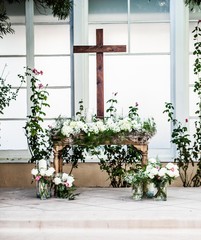 table set for religious wedding ceremony with wood cross and white floral arrangements