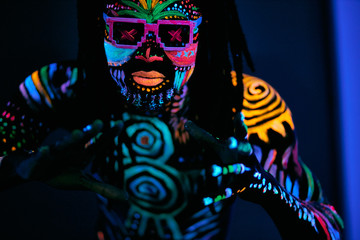 portrait of black african man in fluorescent patterns dancing in ultraviolet light, young dancer with fluorescent glowing makeup move