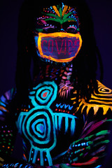 young african male presents himself in the form of coronavirus, wearing mask with fluorescent inscription covid-19. studio shoot