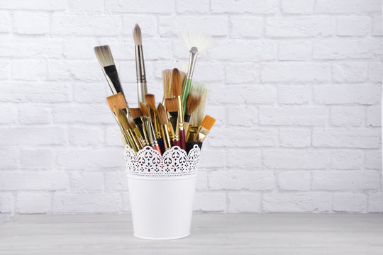 Artist paintbrushes arranged ina white metal bucket isolated on a white brick wall