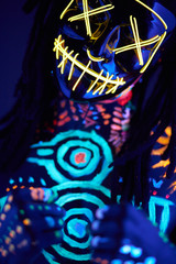 incognito male with fluorescent body art stand in the pose of fighter wearing scary mask. isolated studio shoot