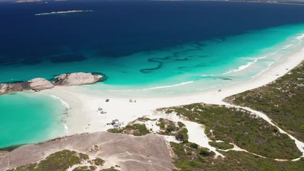 Aerial of Wylie Bay Rock and beach near Esperance on a sunny morning with crystal clear blue water and view of the granite rocks and four wheel drive vehicles on the beach
