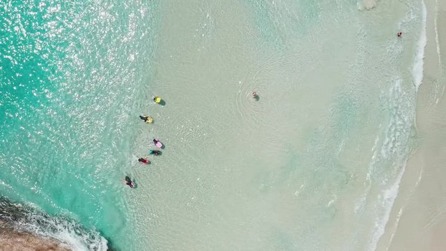 Overhead shot of family and children having fun in the surf and waves at the beach with their colorful body boards in clear turquoise water